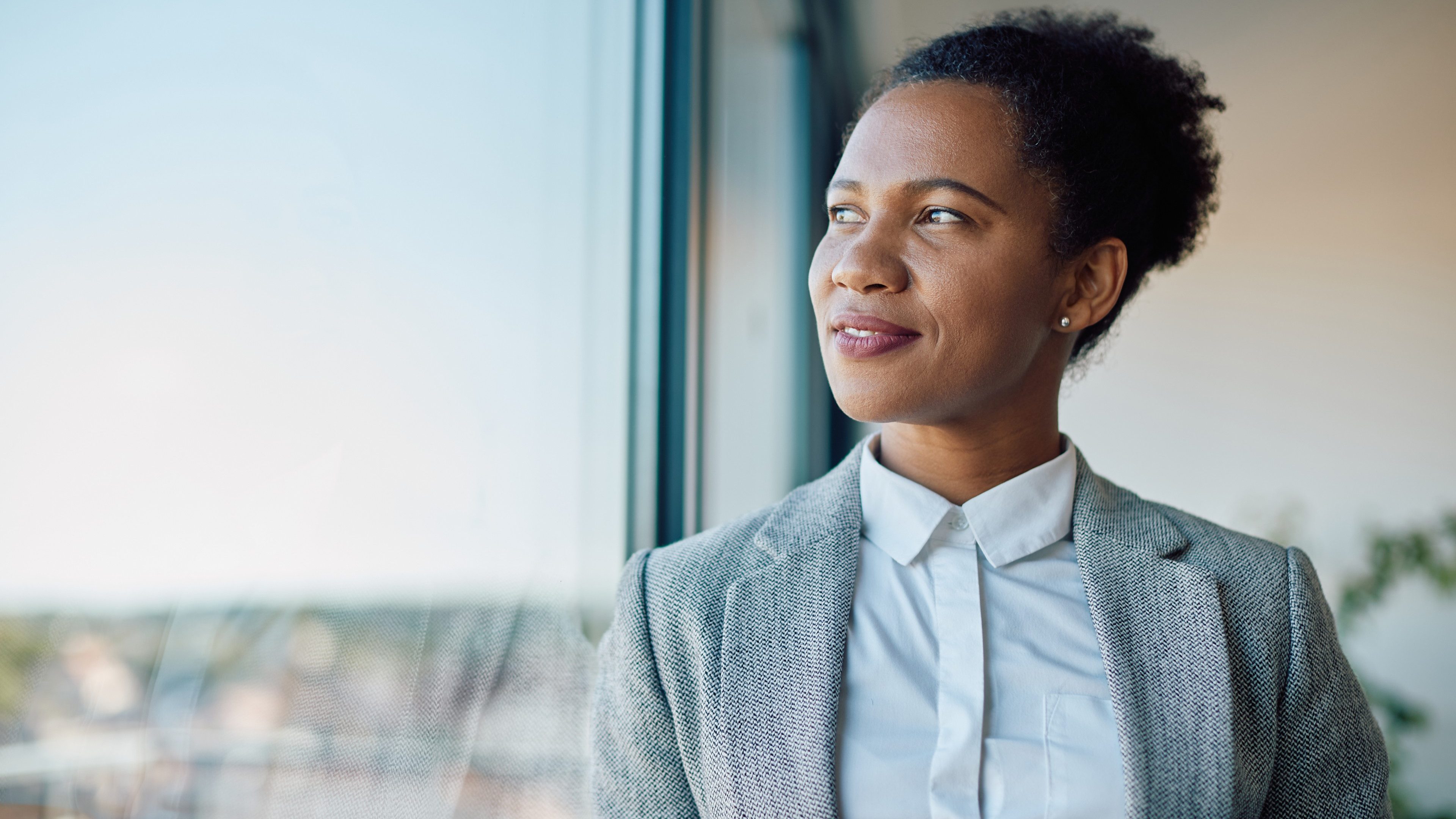 Smiling African American businesswoman looking through the window during her coffee break in the office.