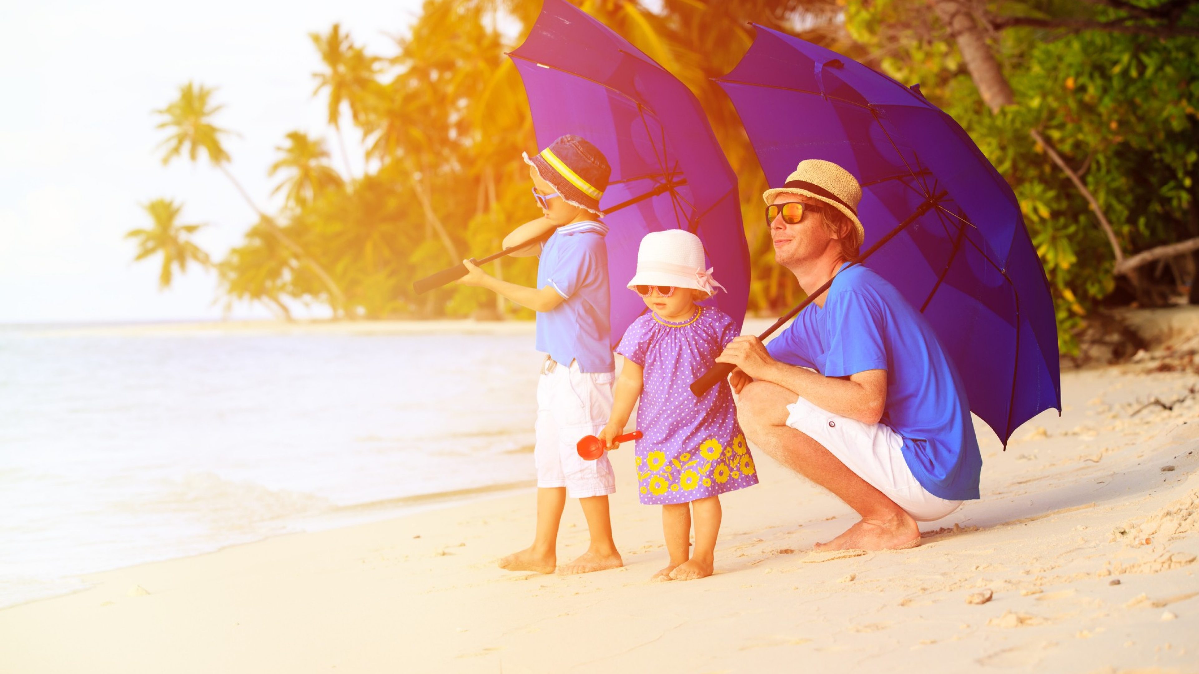 Father and two kids at beach with umbrellas to hide from sun