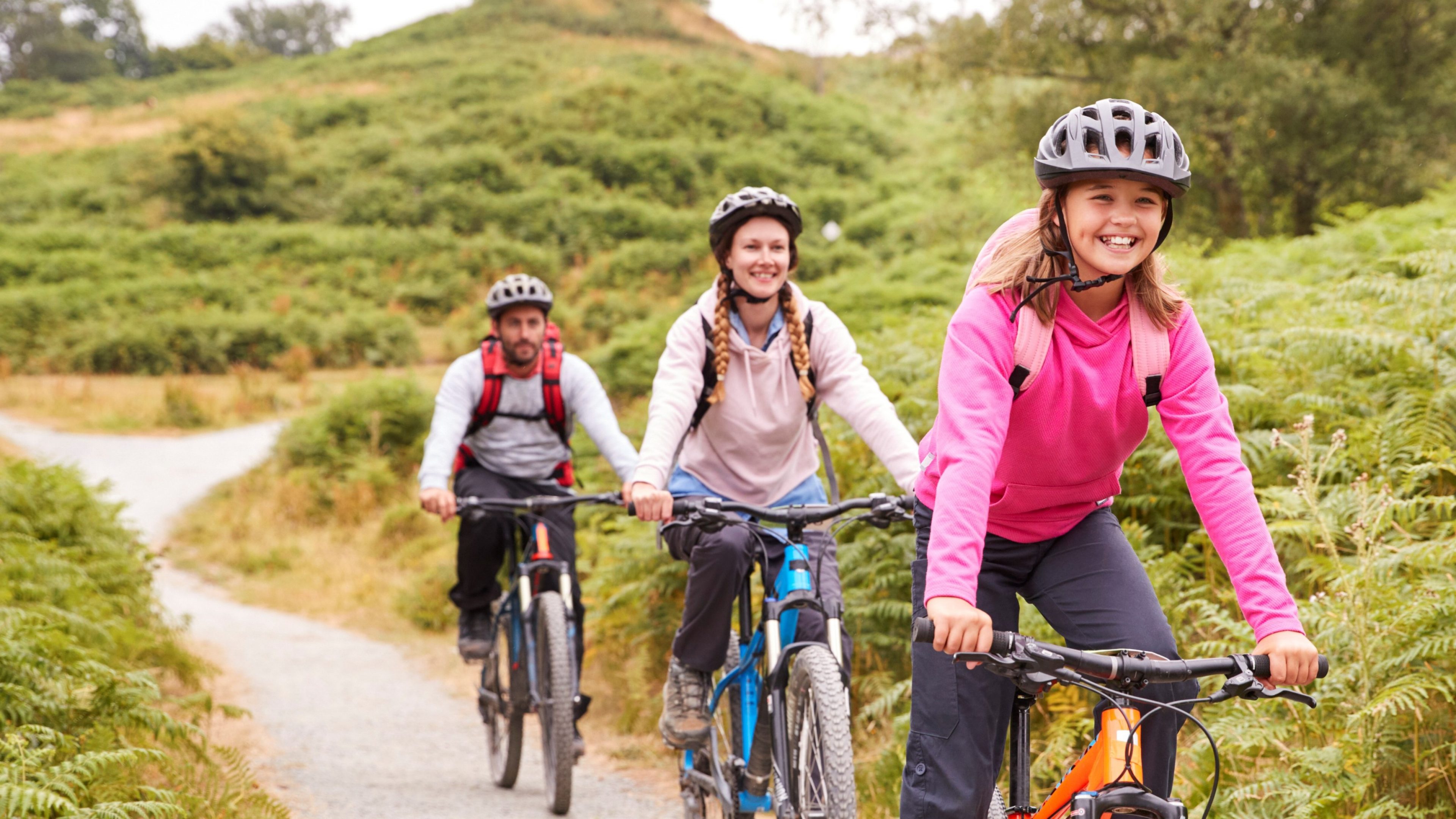 Pre-teen girl riding mountain bike with her parents during a family camping trip, close up