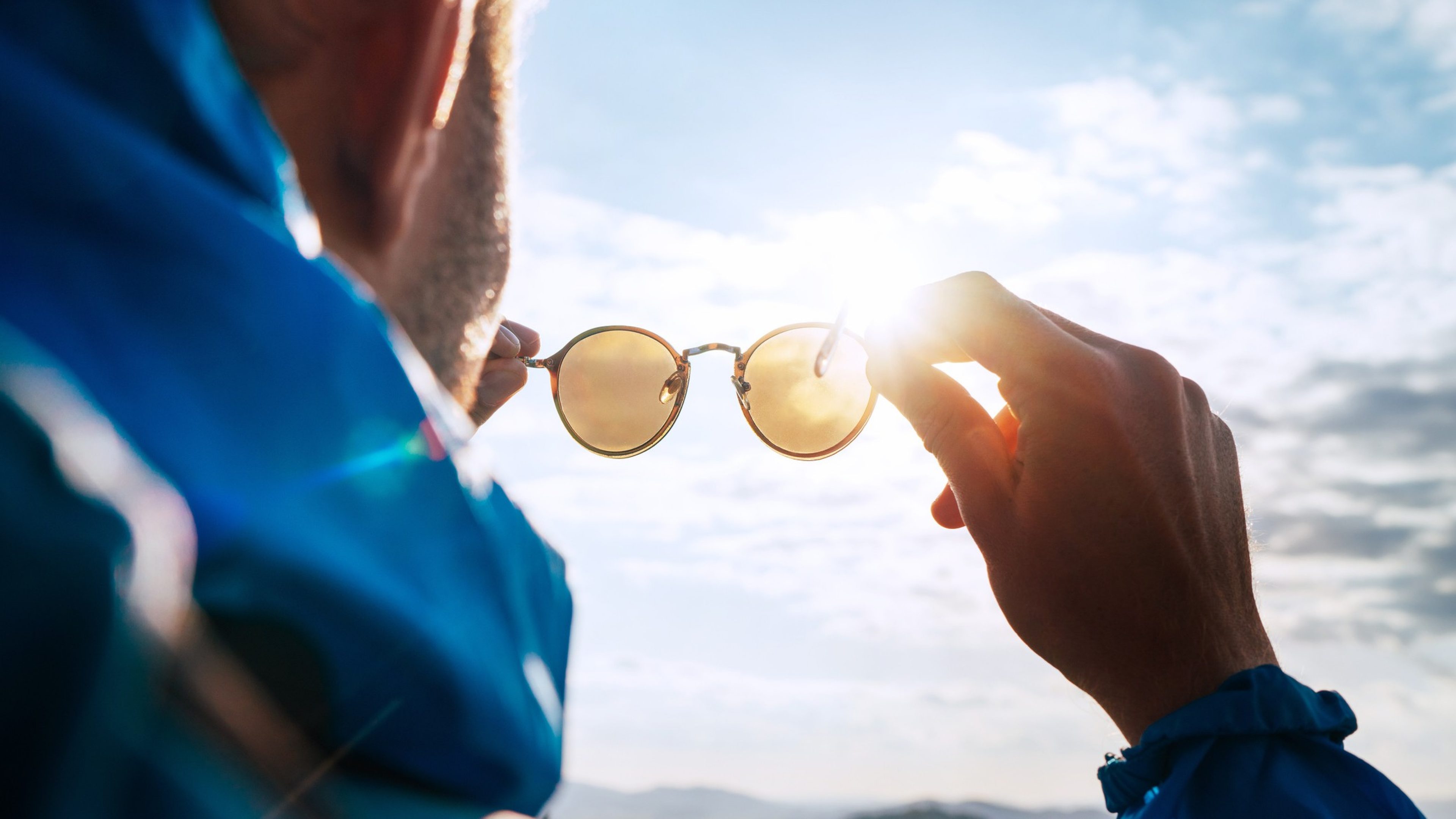 Backpacker man looking at bright sun through polarized sunglasses enjoying mountain landscape. Eye & Vision Care human health concept image.