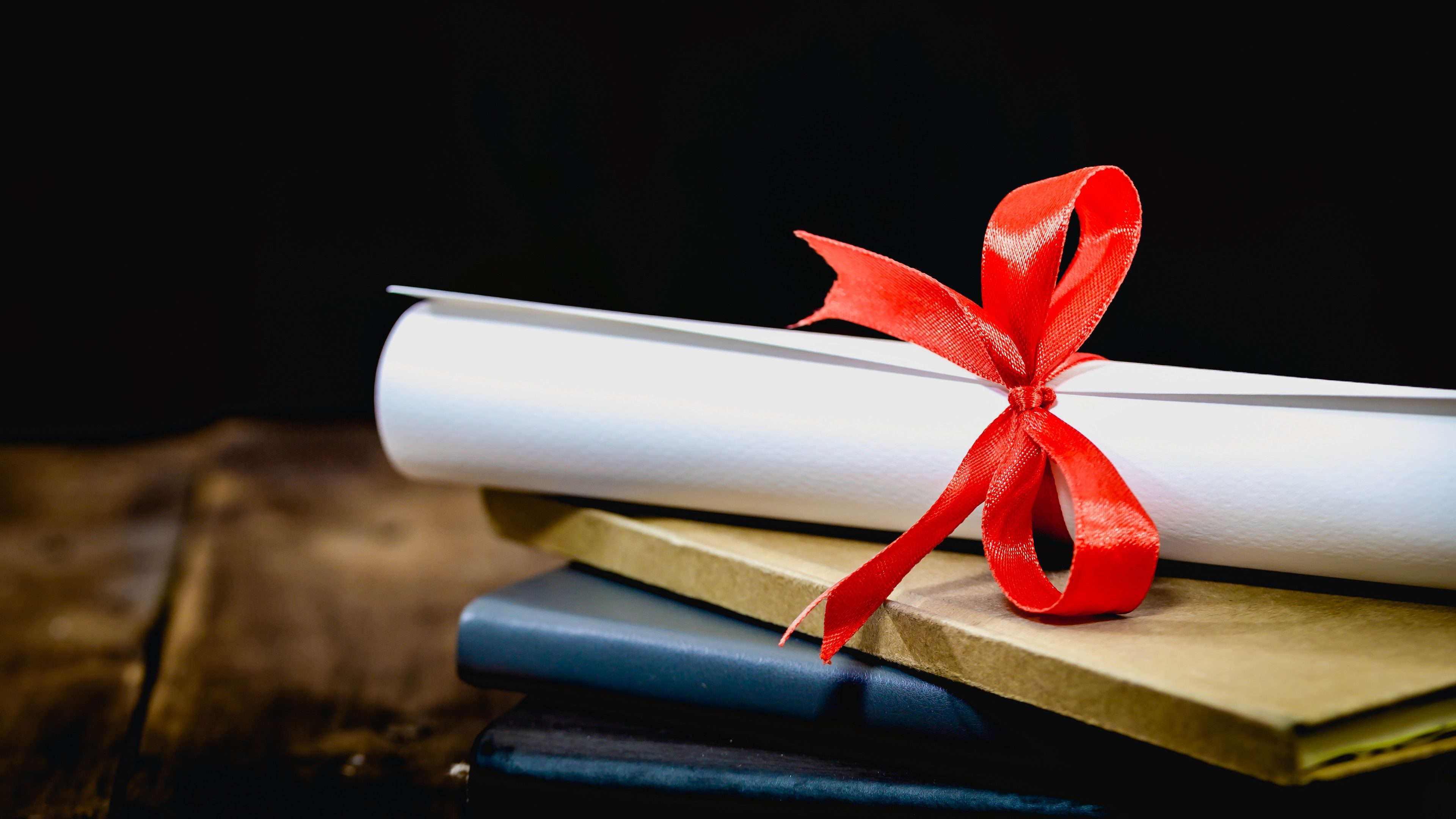 Congratulations for graduating.mortarboard and graduation scroll,tied with red ribbon, on a stack of old battered book with copy space on wood background