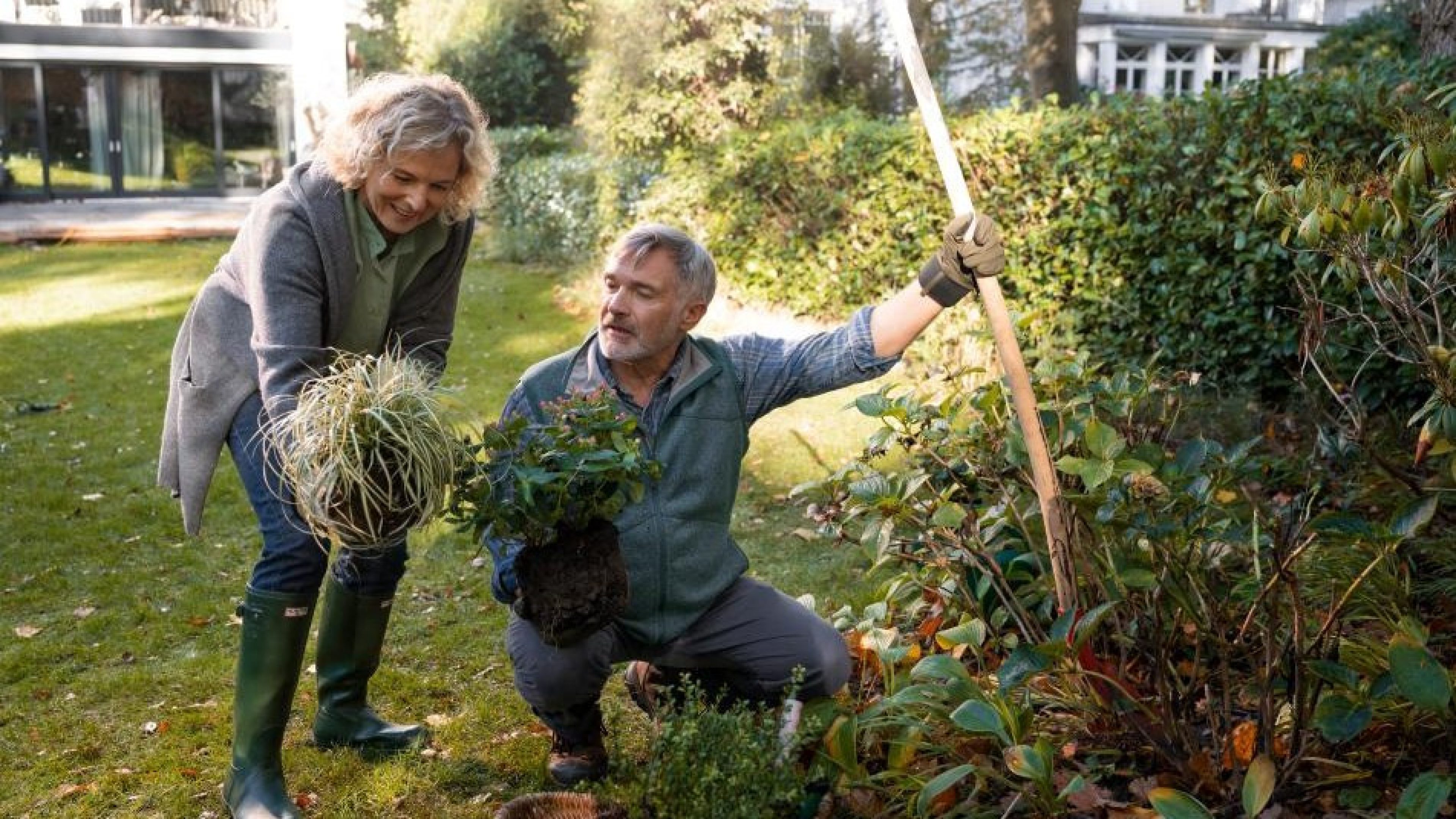 Personnes travaillant dans un jardin, manipulant des plantes et des végétaux à entretenir près d’une maison.