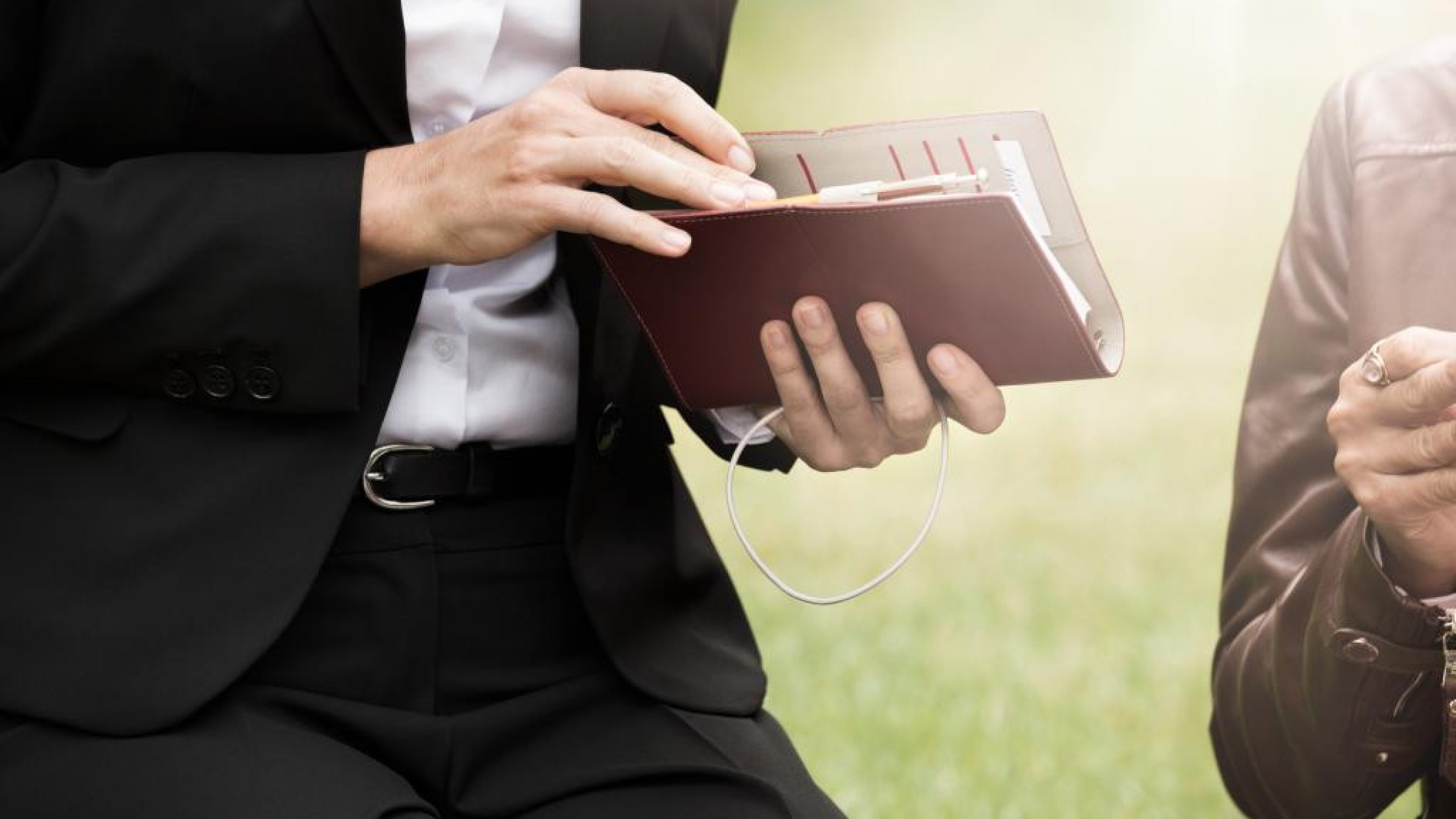 Une personne en costume feuillette un carnet ouvert en extérieur.