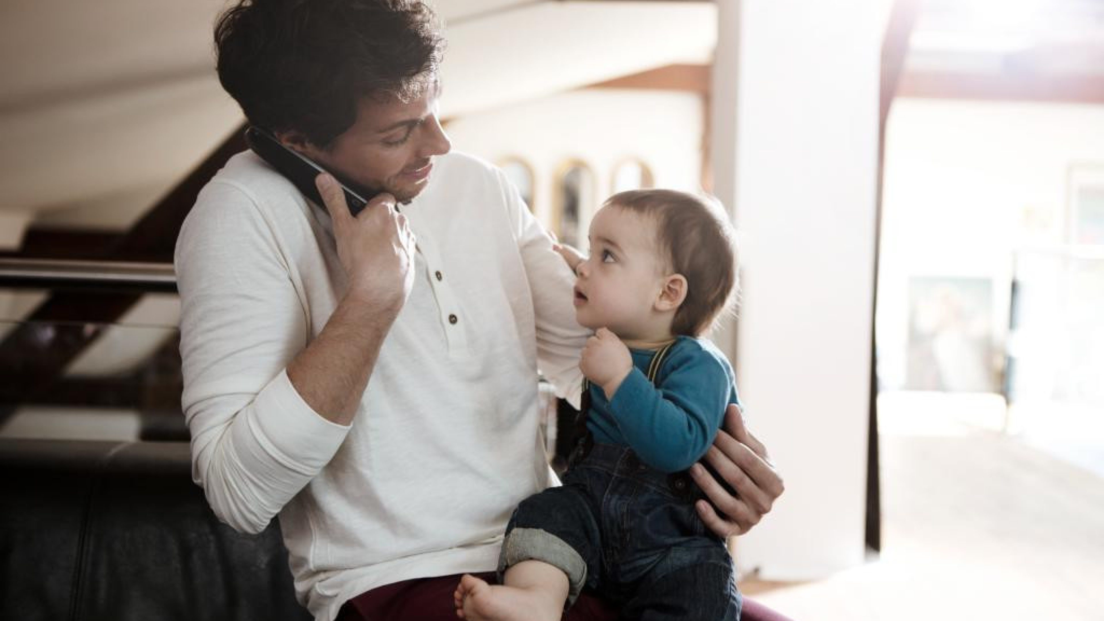 Une personne tient un enfant dans les bras tout en parlant au téléphone.