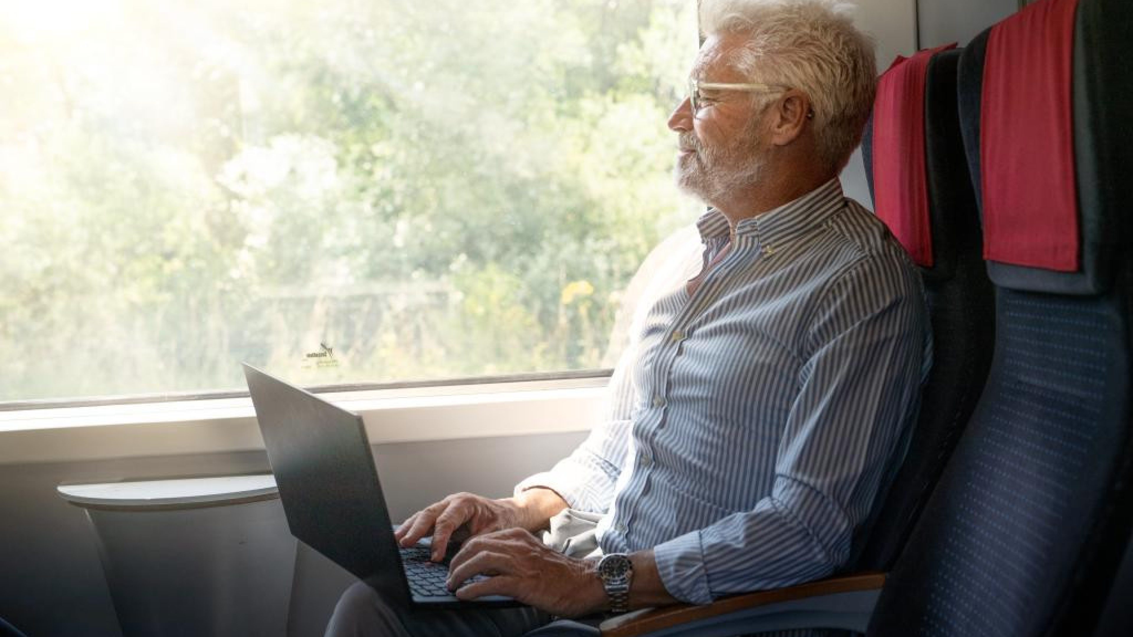 Une personne utilise un ordinateur portable dans un train en regardant par la fenêtre.