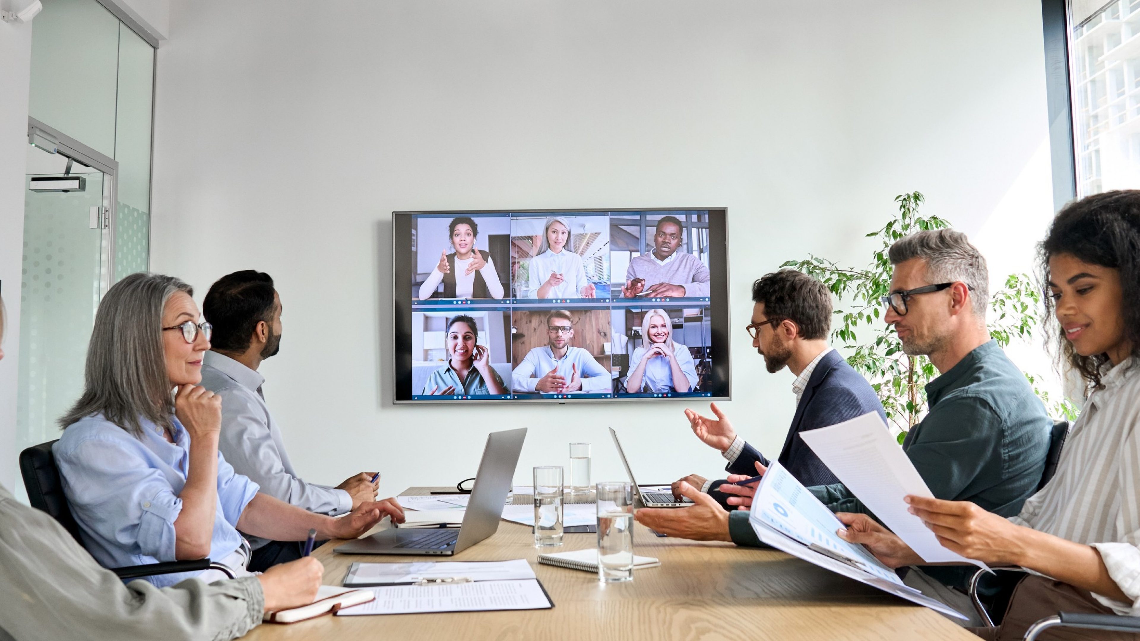 Diverse company employees having online business conference video call on tv screen monitor in board meeting room. Videoconference presentation, global virtual group corporate training concept.