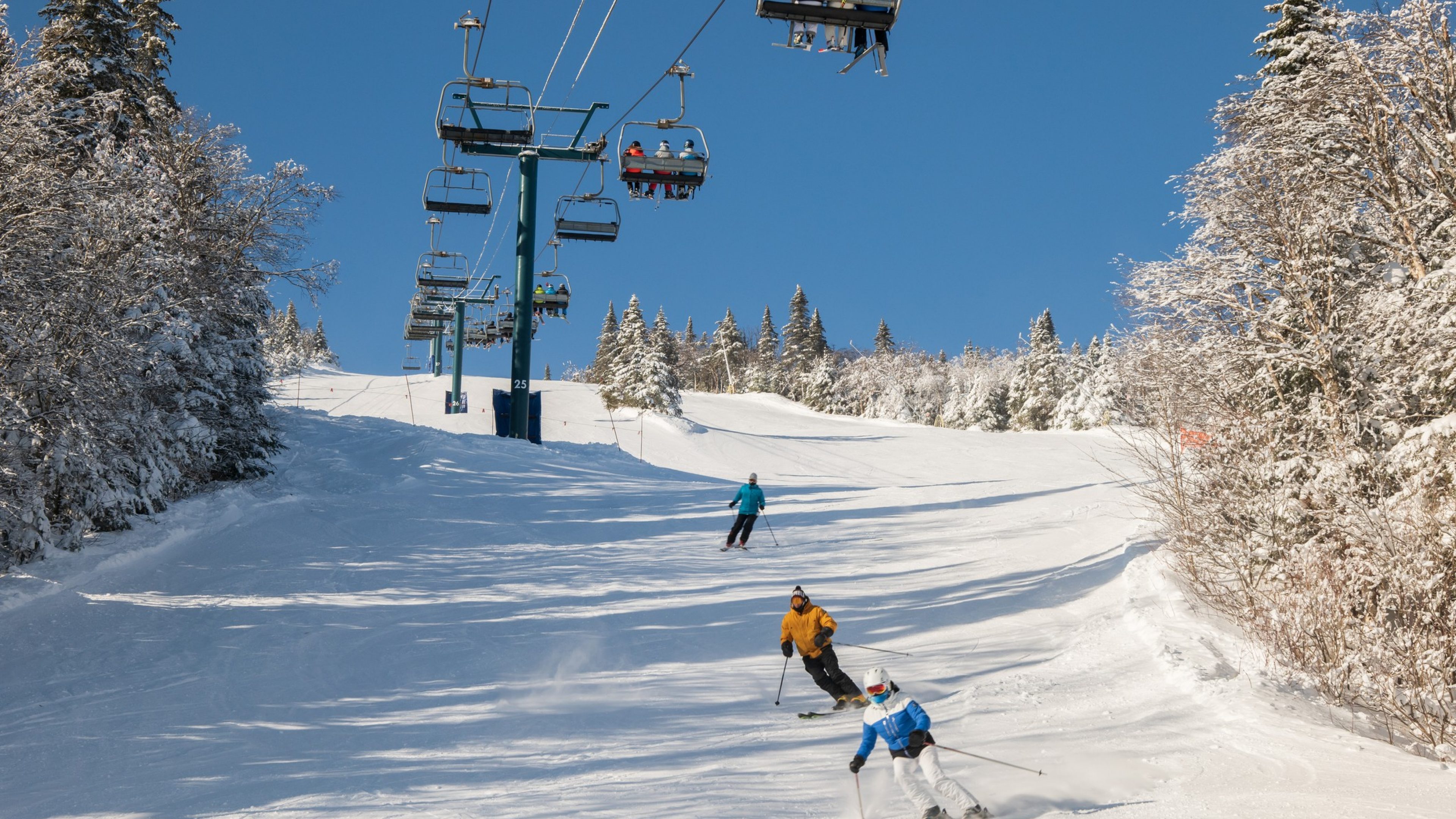 view of skiers climb the ski lift up the hill with snow covered mountains. Ski chairlift climb above the ski slope