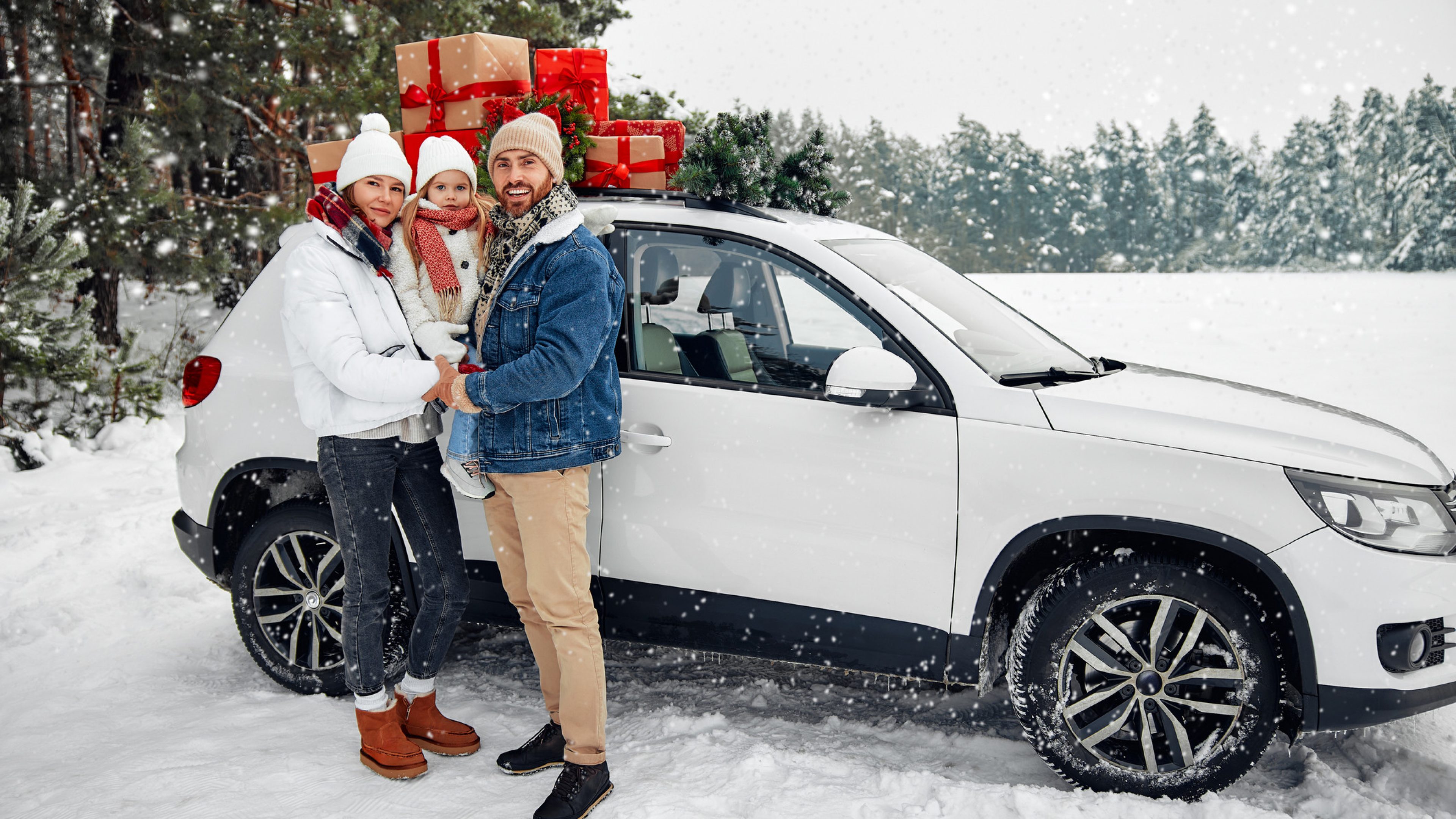 Merry Christmas and New Year. Happy family with a child standing near a car loaded with boxes of gifts against the backdrop of a forest in snowy weather.